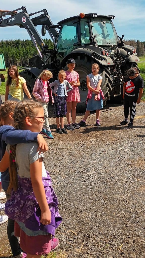 Grundschulkinder stehen vor einem großen Traktor auf dem Lindenhof Kühn in Nisterberg.